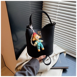 Detail of black lychee grain leather bucket bag with silver clasp and cartoon doll charm