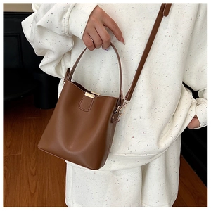 Detail of a brown bucket bag showing the smooth leather texture and golden metal buckle