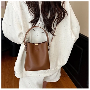 Detailed view of a brown bucket bag with gold buckle and adjustable strap on a model