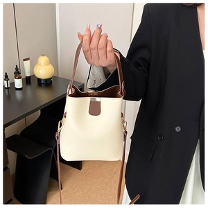 Close-up of a beige bucket bag with brown trim and gold buckle details held by a model
