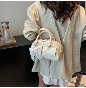 Detail of cream Boston bag with woven texture, lace bow, and pearl charm pendant