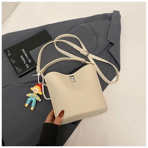 Detail of off-white bucket bag featuring lychee texture, metal clasp, and cartoon pendant