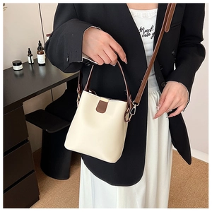 Detail of cream and brown bucket bag with slim handle and gold hardware on model