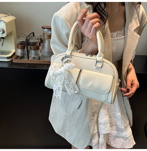 Close-up of cream hand-woven handbag featuring leather pocket and lace pearl bow charm