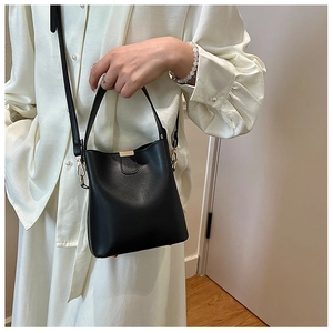 Detail of a black matte bucket bag with gold hardware worn on a white dress