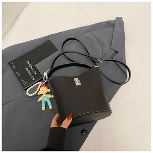 Detail of black lychee texture bucket bag with silver turn-lock and cute doll charm