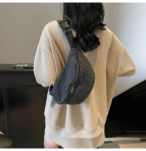 Detail of dark denim crossbody chest bag featuring double zippers and adjustable strap