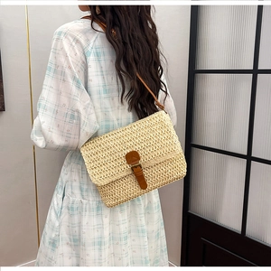 Détail d'un sac bandoulière en paille avec lanière en cuir marron et boucle métal