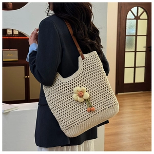 Dettaglio della borsa tote beige intrecciata con motivo a rete e ciondolo floreale