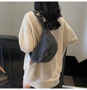 Detailed view of grey denim crescent chest bag with adjustable strap on beige knitwear