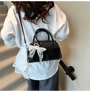 Detail of black woven bowling bag with pearl lace bow charm on a carpeted staircase