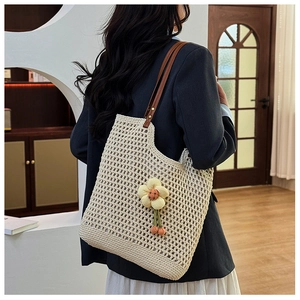 Dettaglio borsa tote beige all'uncinetto con manici in pelle marrone e ciondolo a fiore