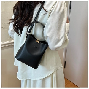 Detail of minimalist black bucket bag featuring golden rectangular buckle and smooth leather texture