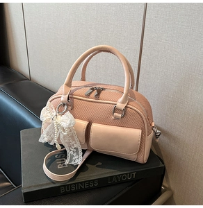 Detail of pink woven handbag featuring lace bow charm and pearl accents on book