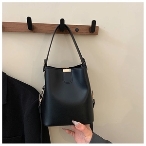Close-up of black bucket bag with golden hardware hanging on a wooden wall hook
