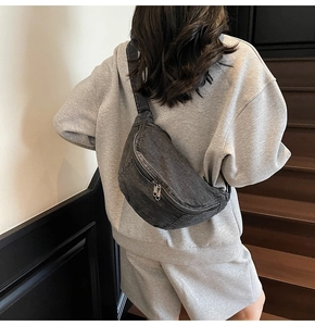 Close-up of casual denim sling bag with dual zippers worn over a grey sweatshirt