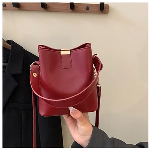 Detail of dark red bucket bag featuring matte leather texture and gold metal buckle