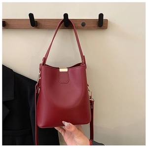 Detail view of red bucket bag with smooth texture and golden metal buckle hardware