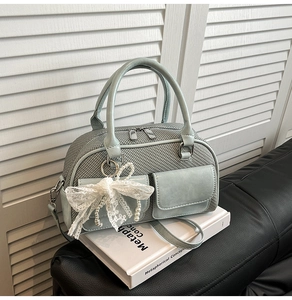 Detail of light blue bowling bag featuring lace bow, pearl charm, and woven texture