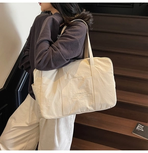Detail of off-white canvas tote bag featuring motivational embroidery and side pocket