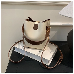 Detail of minimalist cream bucket bag with brown trim and elegant gold metal buckle hardware