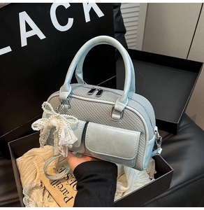 Detailed view of gray-blue handbag with pearl lace bow charm in a gift box