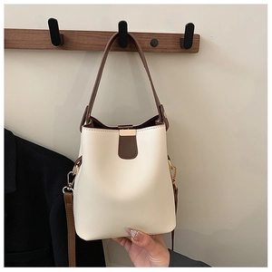 Detail of cream bucket bag featuring brown leather trim and metallic buckle closure