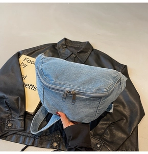 Detail of blue denim crescent chest bag with double metal zippers and denim strap