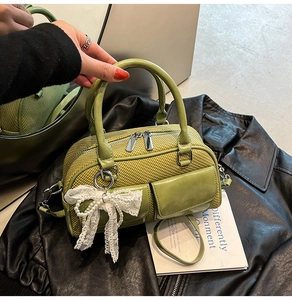 Close-up of grass green woven handbag with pearl bow charm and twin front pockets