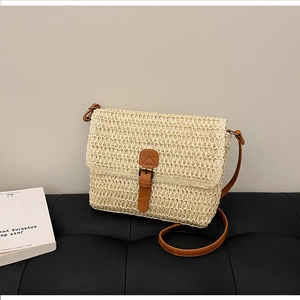 Détail d'un sac bandoulière en paille tissée avec fermoir en cuir marron sur cuir noir