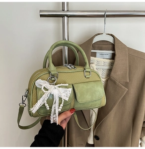 Detail of green straw and leather bowling bag with pearl lace bow charm hanging on rack