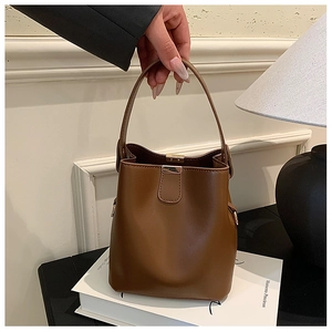 Detail of caramel brown bucket bag with shiny leather texture and golden metal buckle