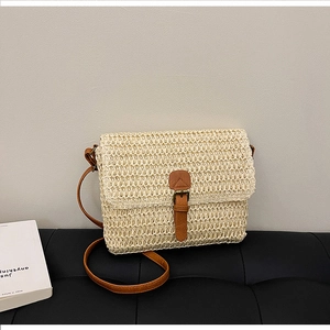 Détail du sac bandoulière en paille tressée avec lanière en cuir marron sur surface texturée