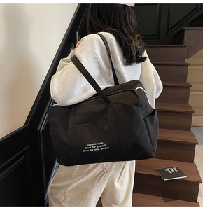 Detailed close-up of large black canvas tote bag with white inspirational text on the strap