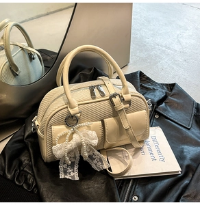 Detail of cream bowling bag with woven texture and pearl bow charm on a leather jacket