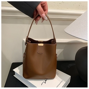 Detailed view of dark brown leather bucket bag featuring gold metal hardware and top handle