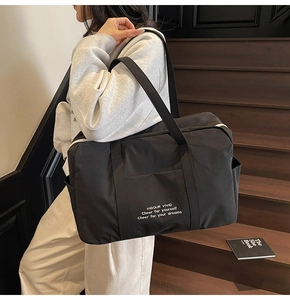 Detail of a black large capacity nylon travel tote bag featuring vivid white typography print