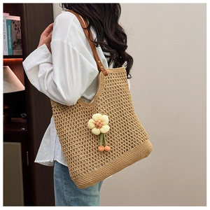 Dettaglio della borsa tote in paglia intrecciata con spalline in pelle e ciondolo
