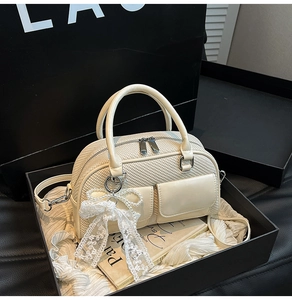 Detail of cream bowling bag with woven texture, pearl bow and lace in a gift box