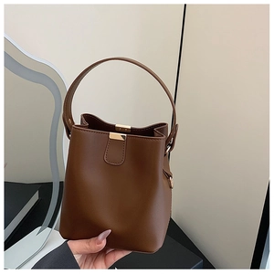 Detail shot of brown leather bucket bag featuring gold hardware and rigid top handle