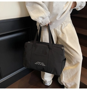 Detail of a large black nylon tote bag with white lettering on a modern wooden staircase
