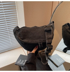 Detailed close-up of a black denim crescent bag featuring metal zippers and wide strap