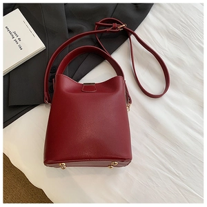 Detailed view of burgundy leather bucket bag with metal feet on a textured white fabric
