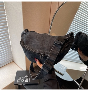 Detail of black washed denim crescent bag featuring metal zipper and wide nylon strap