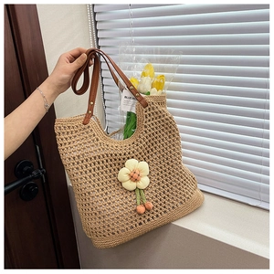 Dettaglio borsa tote beige intrecciata a mano con ciondoli floreali e manici in pelle