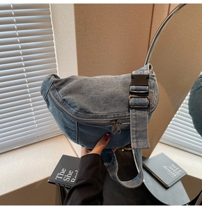 Detail of blue denim crescent crossbody bag featuring dual zippers and adjustable strap
