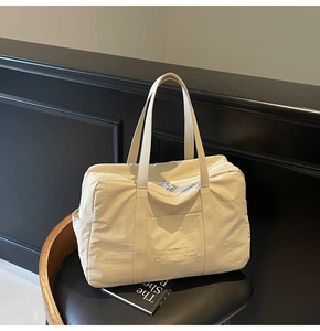 Detailed close-up of cream canvas travel tote with contrast embroidery on a black chair