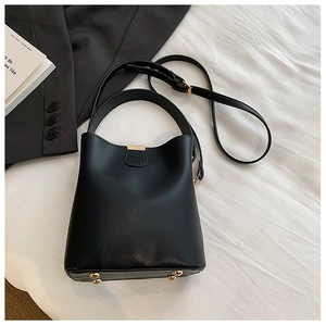 Detail of black leather bucket bag with gold hardware feet and adjustable shoulder strap