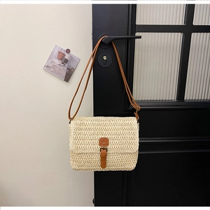 Détail d'un sac bandoulière en paille tressée beige avec sangle en cuir sur une poignée de porte