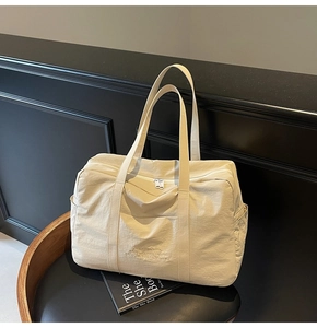 Detail of beige wrinkled nylon tote with dual zippers and custom embroidery